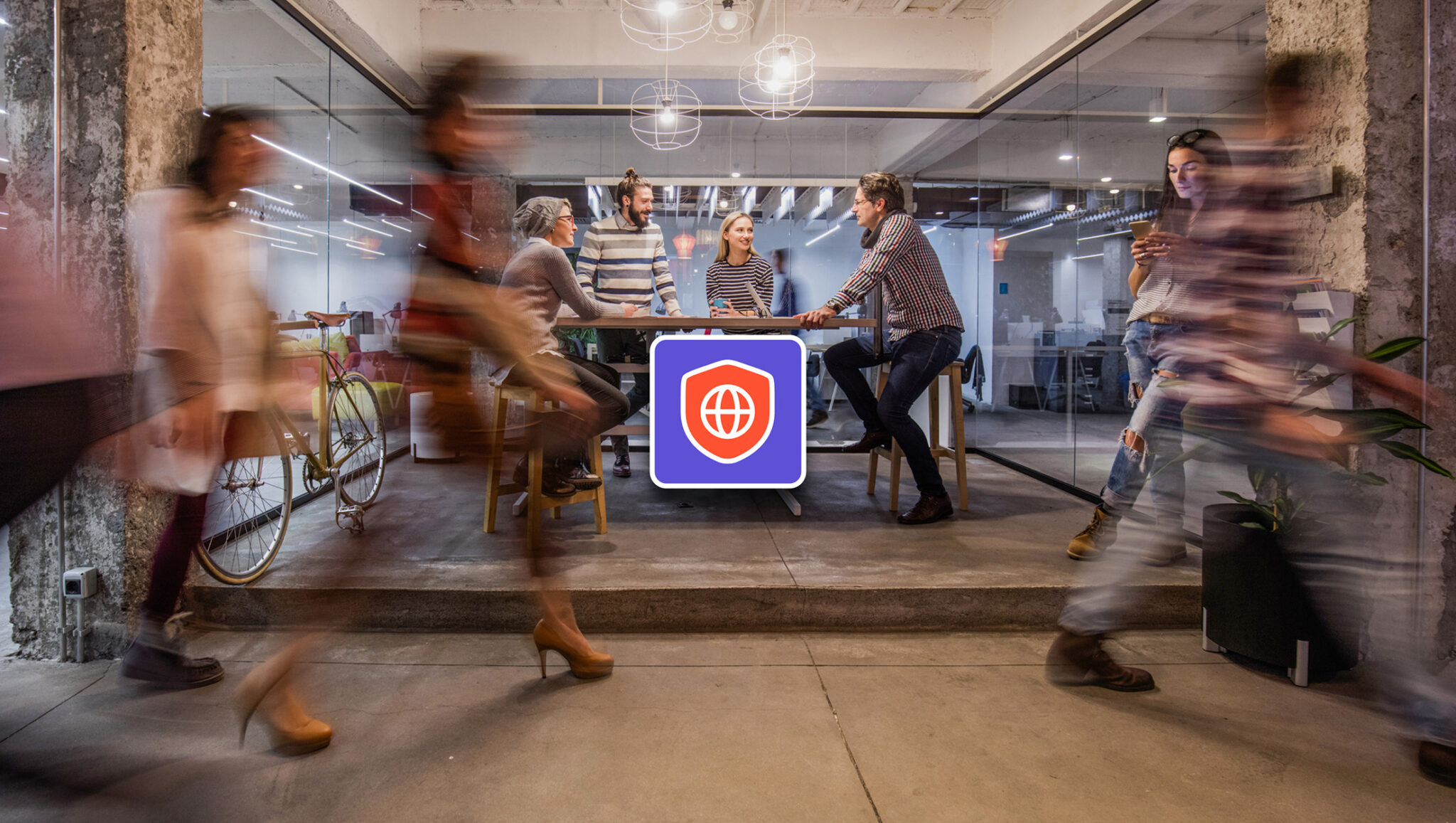 A group of people in a modern coworking space talking and working, with others walking past in the foreground.